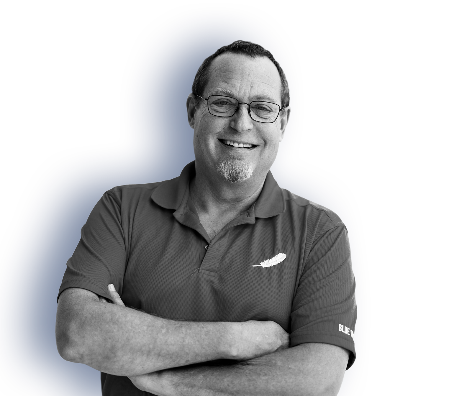 A man in glasses wearing a polo shirt with a Blue Origin feather logo stands with his arms crossed in front of his chest.